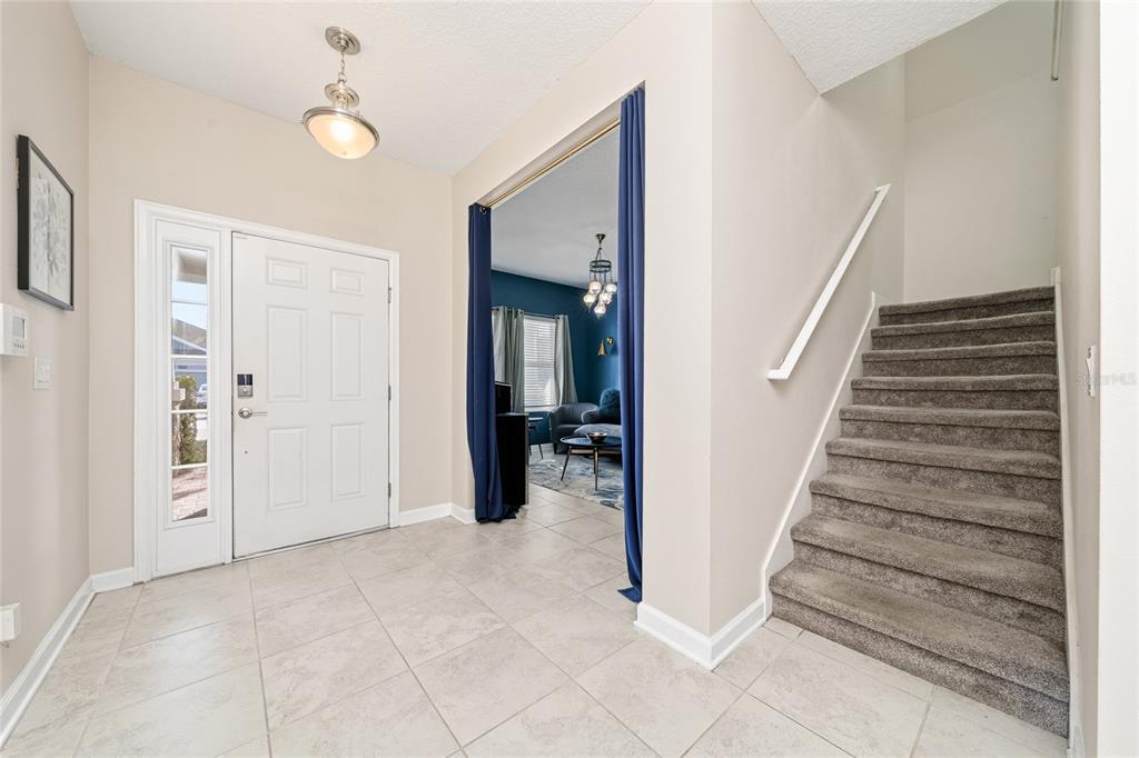 An entryway features tile flooring, a white front door, a carpeted staircase, and blue curtains — 11059 LONGLEAF WOODS DRIVE, ORLANDO, FL