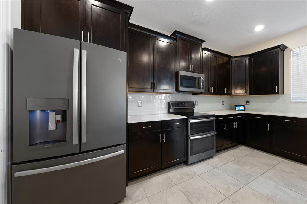 A kitchen features dark wood cabinets, stainless steel appliances, white countertops, and a tile floor — 11059 LONGLEAF WOODS DRIVE, ORLANDO, FL