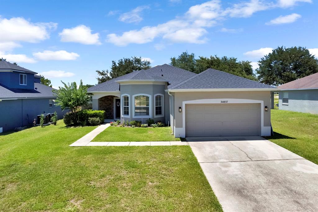 A single-story suburban house with a gray exterior, a two-car garage, and a front lawn — 34037 FORTUNADO STREET, SORRENTO, FL