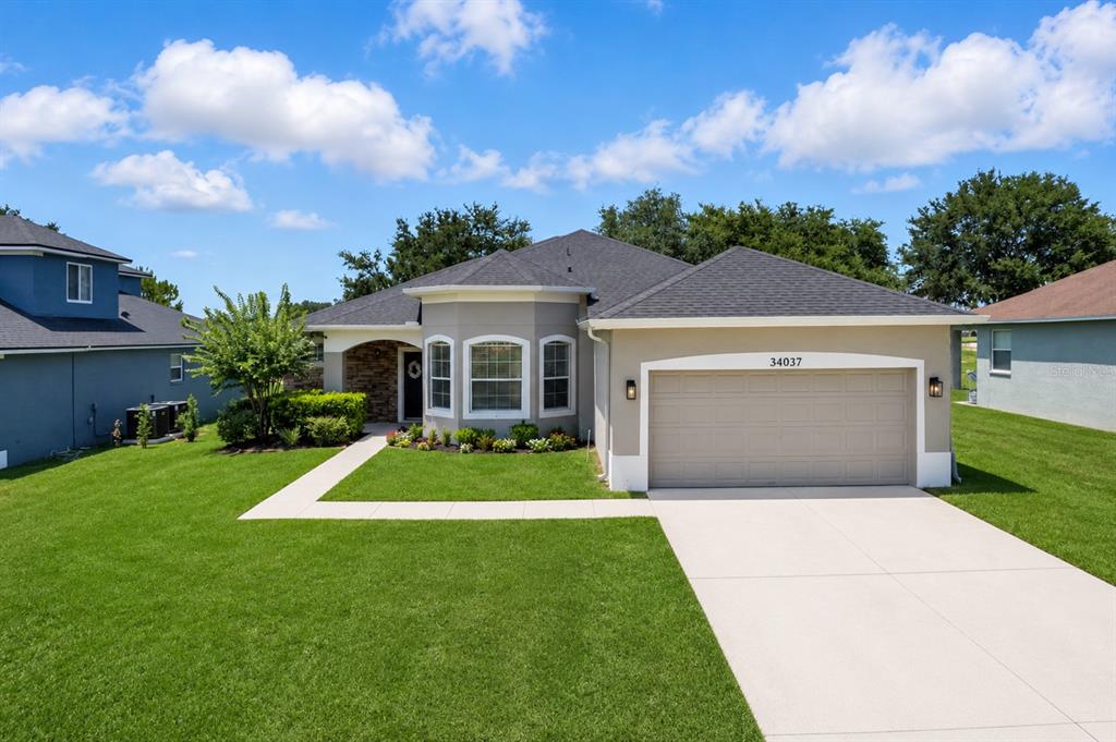 A single-story suburban house features a gray exterior, a two-car garage, and a front lawn — 34037 FORTUNADO STREET, SORRENTO, FL