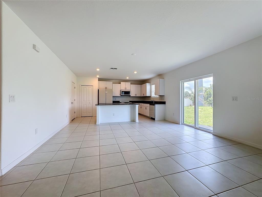 An open-concept kitchen with white cabinets and a center island overlooks a tiled living area — 2739 RED EGRET DRIVE, BARTOW, FL