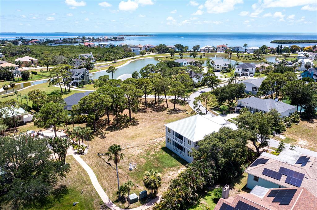 An aerial view shows a coastal neighborhood with houses, a pond, and a large body of water — OTTER CT, TARPON SPRINGS, FL