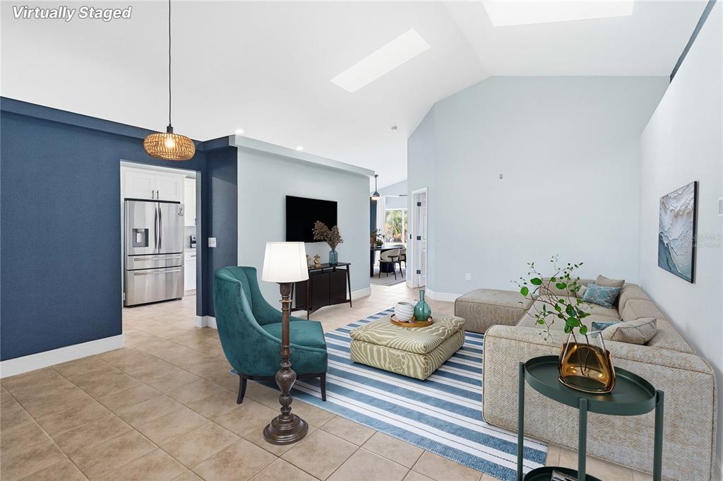 This virtually staged living room features a vaulted ceiling, tile flooring, and blue accent walls — 535 CORNWALLIS DRIVE, DAVENPORT, FL