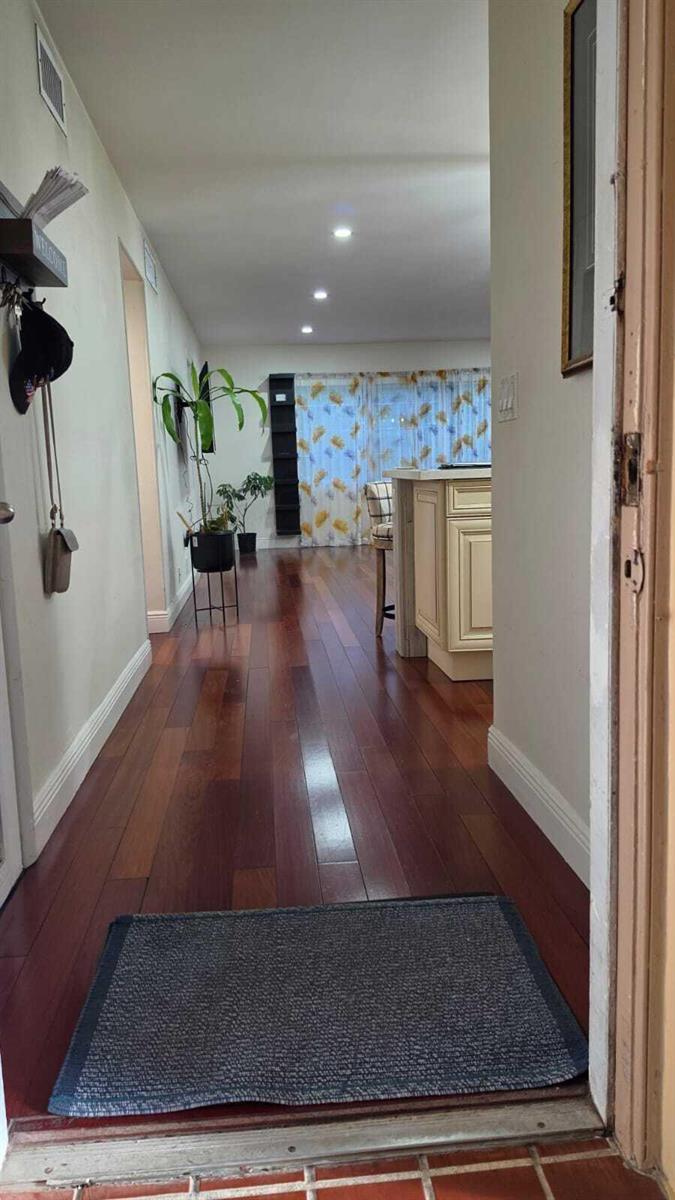 A hallway with dark wood flooring leads to a kitchen area with a center island — 100 Ashbury Road # 206, Hollywood FL 33024, HOLLYWOOD, FL