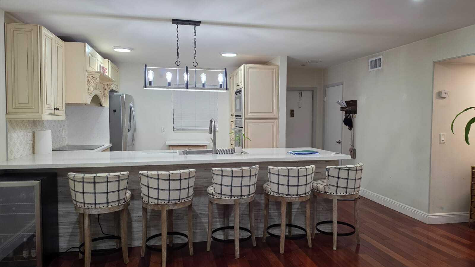 A kitchen features a white quartz island with five plaid barstools and cream-colored cabinetry — 100 Ashbury Road # 206, Hollywood FL 33024, HOLLYWOOD, FL