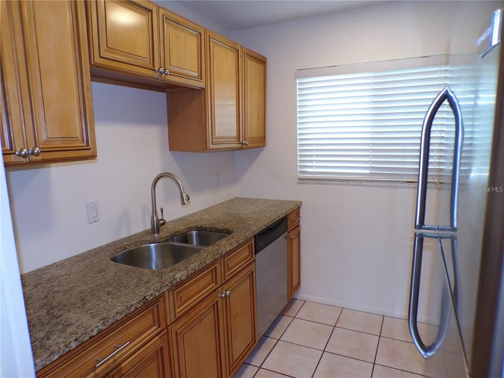 A kitchen features light wood cabinets, granite countertops, a stainless steel sink, and tile flooring — 649 S TAMIAMI TRAIL S UNIT 304, VENICE, FL