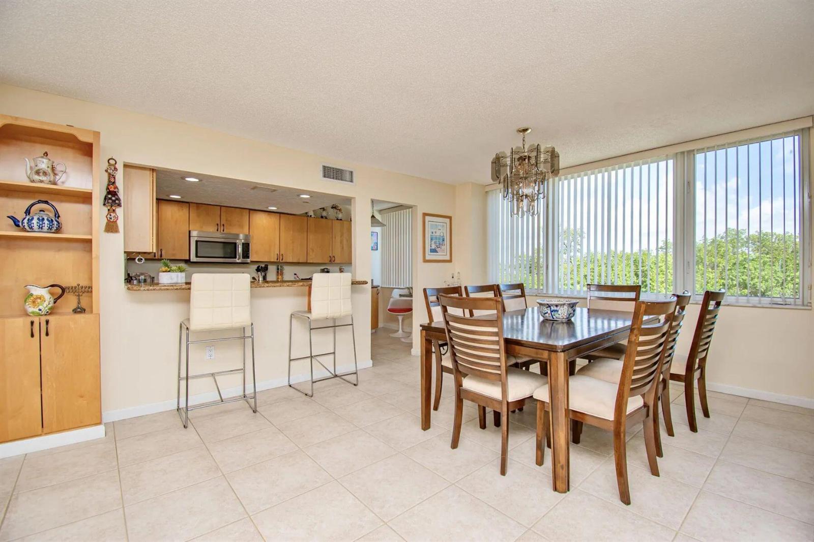 A dining area with a wooden table and chairs, adjacent to a kitchen with bar seating — 3912 S Ocean Boulevard, Highland Beach FL 33487, HIGHLAND BEACH, FL