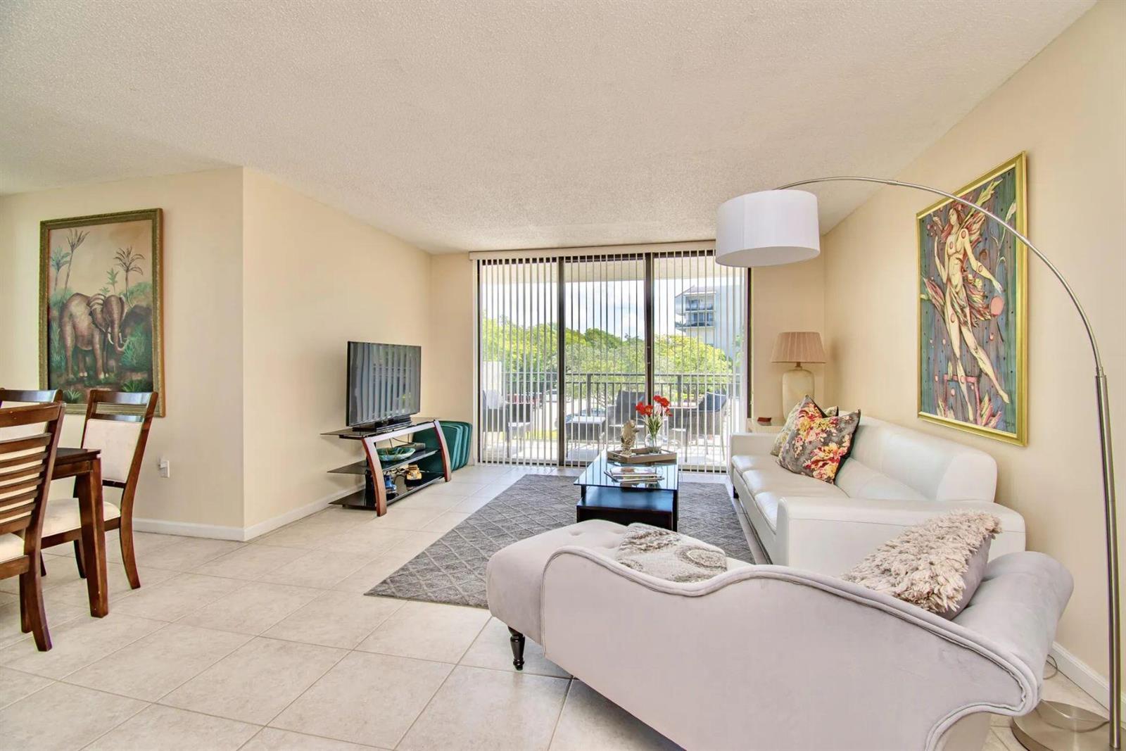 A living room features a white sofa, a chaise lounge, tile floors, and a balcony — 3912 S Ocean Boulevard, Highland Beach FL 33487, HIGHLAND BEACH, FL