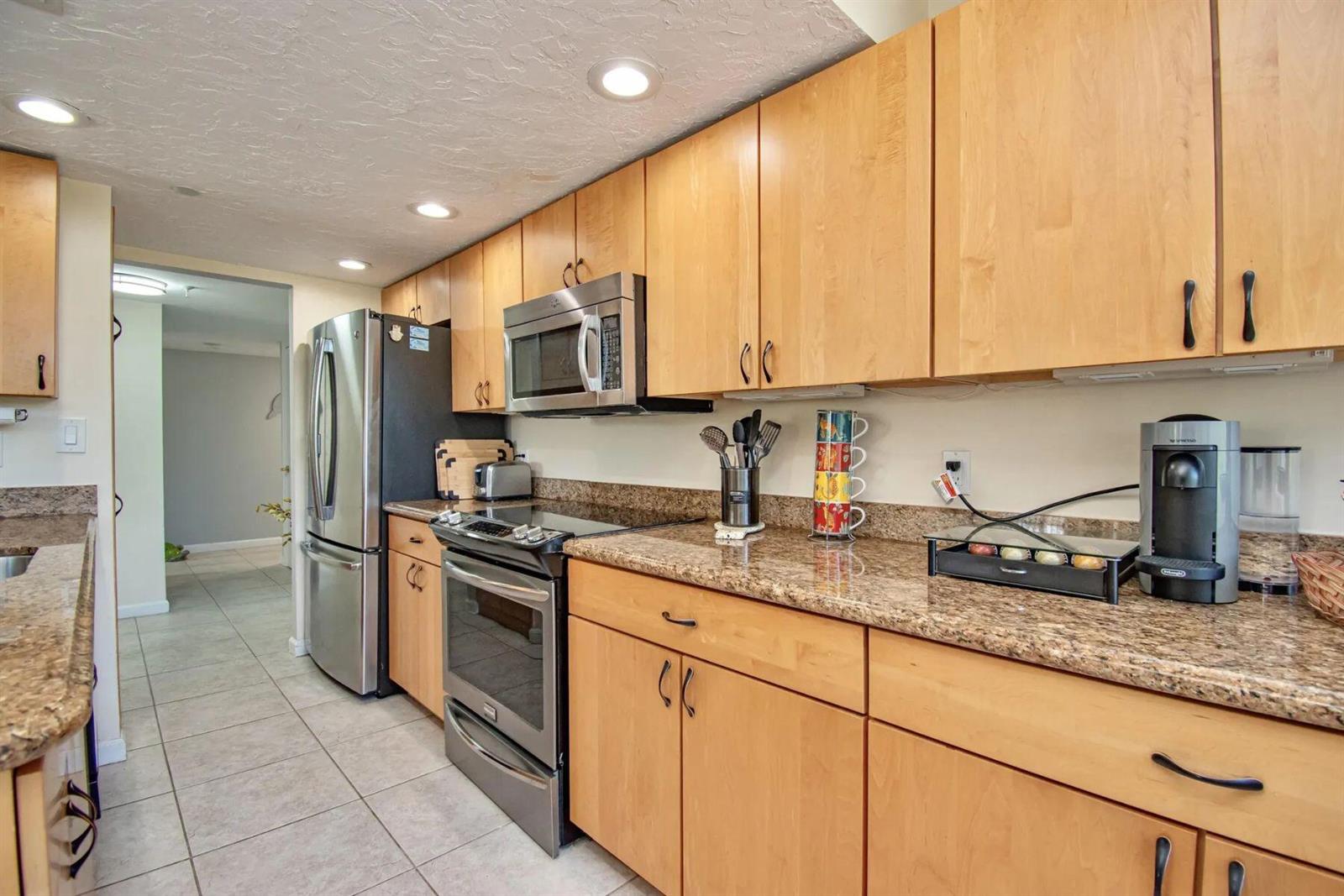 A kitchen features light wood cabinets, granite countertops, and stainless steel appliances — 3912 S Ocean Boulevard, Highland Beach FL 33487, HIGHLAND BEACH, FL