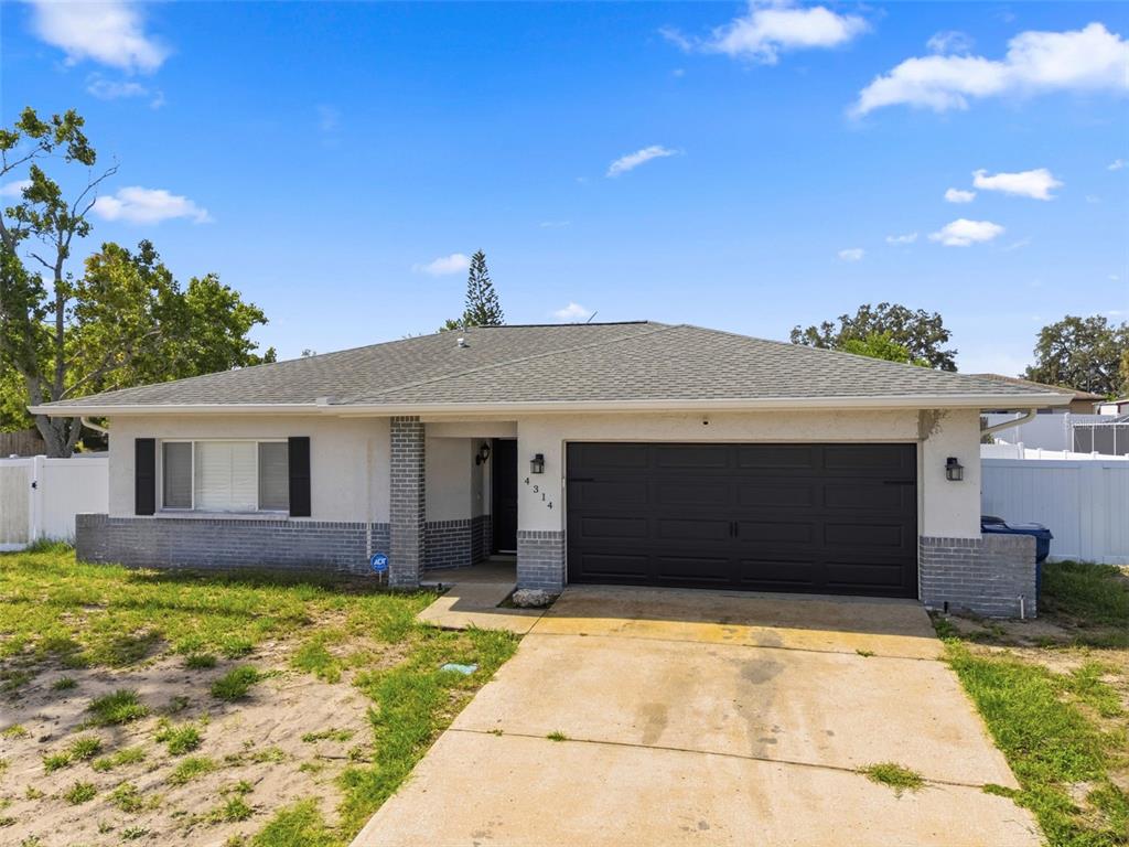 A single-story house with a gray brick base, white stucco walls, and a black garage door — 4314 PINEFIELD AVENUE, HOLIDAY, FL