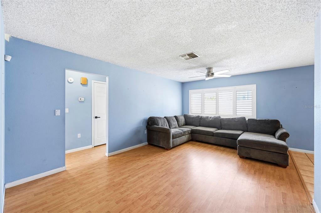 A living room with light blue walls, wood-look flooring, and a large grey sectional sofa — 4314 PINEFIELD AVENUE, HOLIDAY, FL