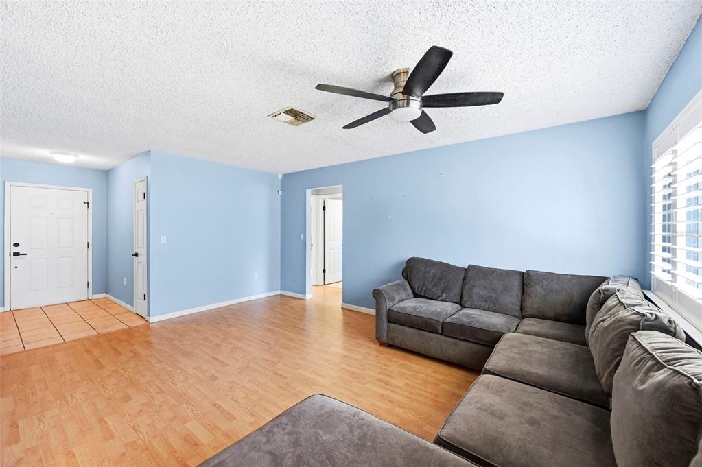 A living room features light blue walls, wood-look flooring, a ceiling fan, and a sectional sofa — 4314 PINEFIELD AVENUE, HOLIDAY, FL