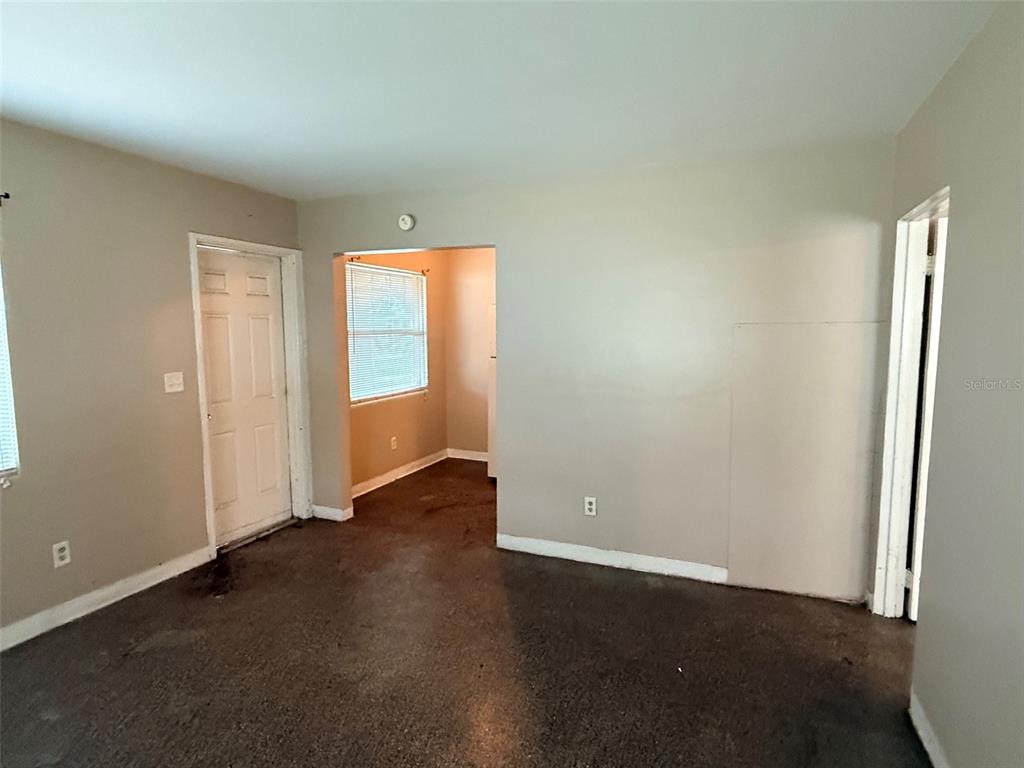 An empty room with beige walls, a white door, and dark flooring — 1273 S BETTY LANE, CLEARWATER, FL