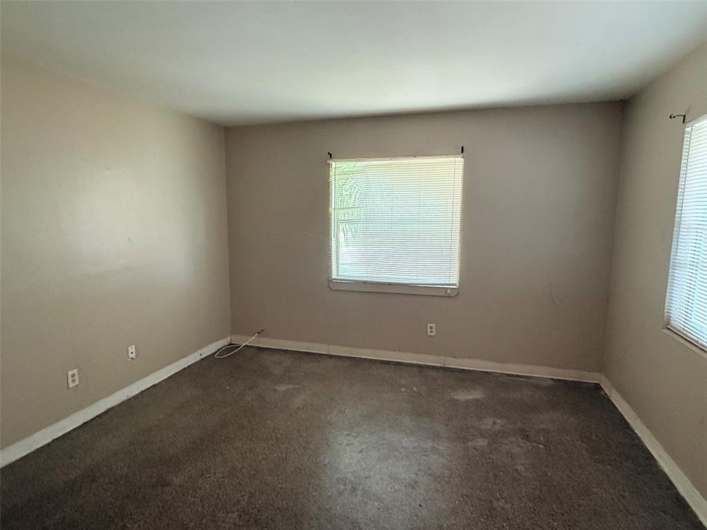 An empty bedroom features beige walls, gray carpeting, and two windows with white blinds — 1273 S BETTY LANE, CLEARWATER, FL