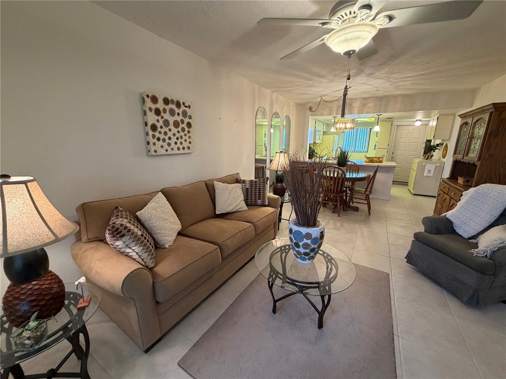 A living room with a tan sofa, glass coffee table, and an adjacent dining area — 25225 RAMPART BOULEVARD UNIT 2203, PUNTA GORDA, FL