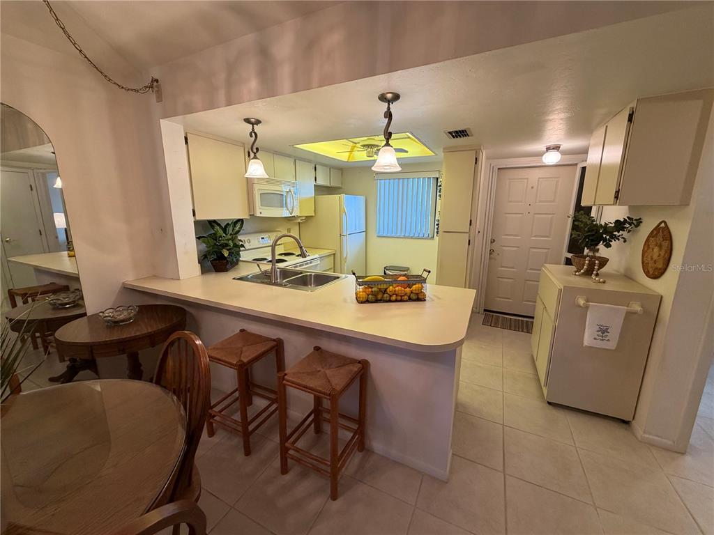 A kitchen features a breakfast bar, light-colored cabinets, tile flooring, and a pass-through window — 25225 RAMPART BOULEVARD UNIT 2203, PUNTA GORDA, FL