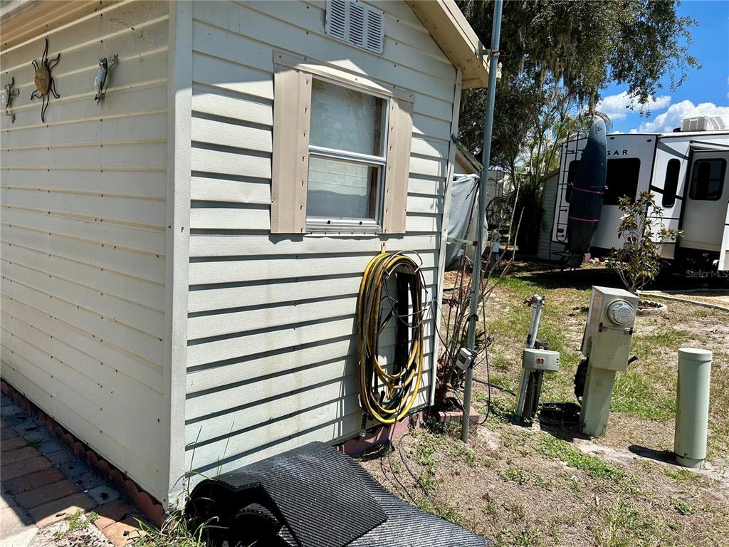 The exterior of a light-colored shed features a window, a coiled hose, and utility equipment — 2928 BIRDIE DRIVE, BOWLING GREEN, FL