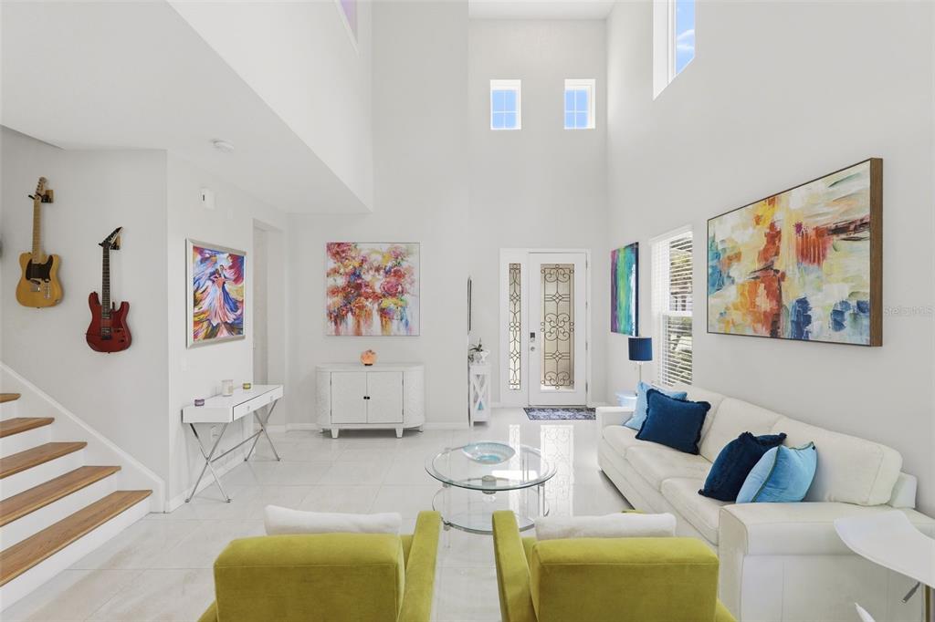 A bright, high-ceilinged living room features white tile floors, a white sofa, and two lime-green chairs — 1418 LONE FEATHER TRAIL, WINTER PARK, FL