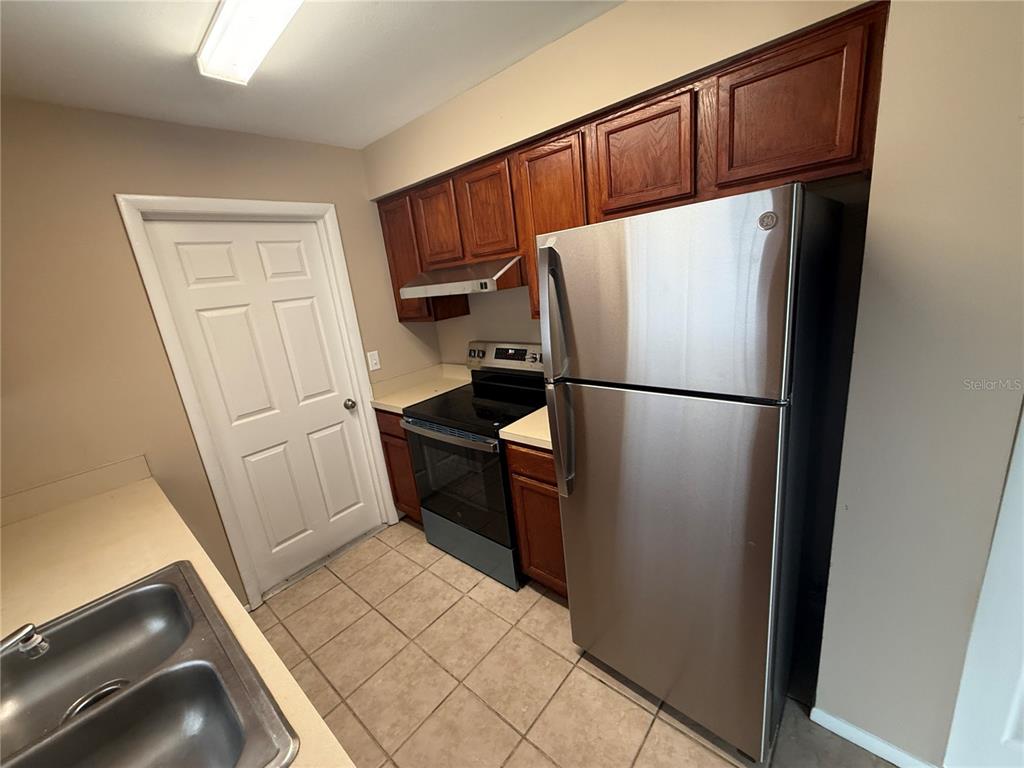 A kitchen features wood cabinets, stainless steel appliances, a tile floor, and a white door — 423 LONGWOOD CIRCLE, LONGWOOD, FL
