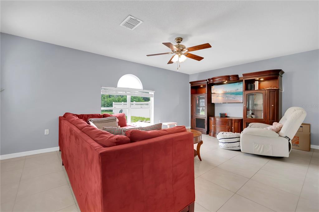 A living room features light gray walls, tile flooring, a red sofa, and a wooden entertainment center — 10304 RIVER BREAM DRIVE, RIVERVIEW, FL