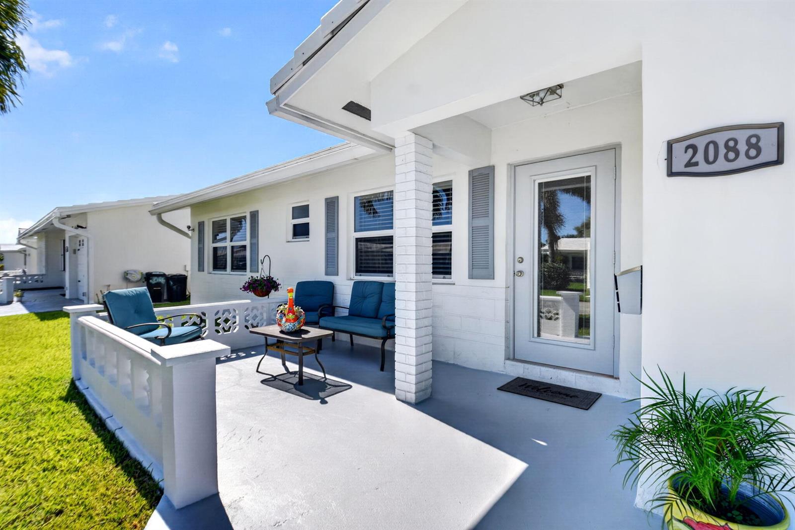 A white house exterior features a covered front porch with blue furniture and a door — 2088 SW 13th Terrace, Boynton Beach FL 33426, BOYNTON BEACH, FL