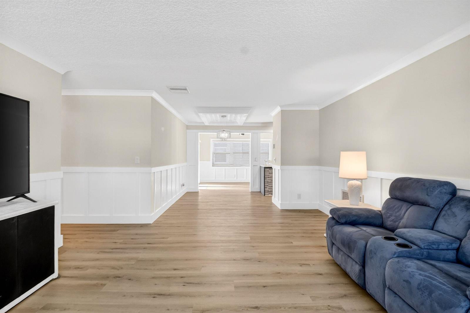A living room features light wood flooring, white wainscoting, a blue recliner, and a television — 2088 SW 13th Terrace, Boynton Beach FL 33426, BOYNTON BEACH, FL