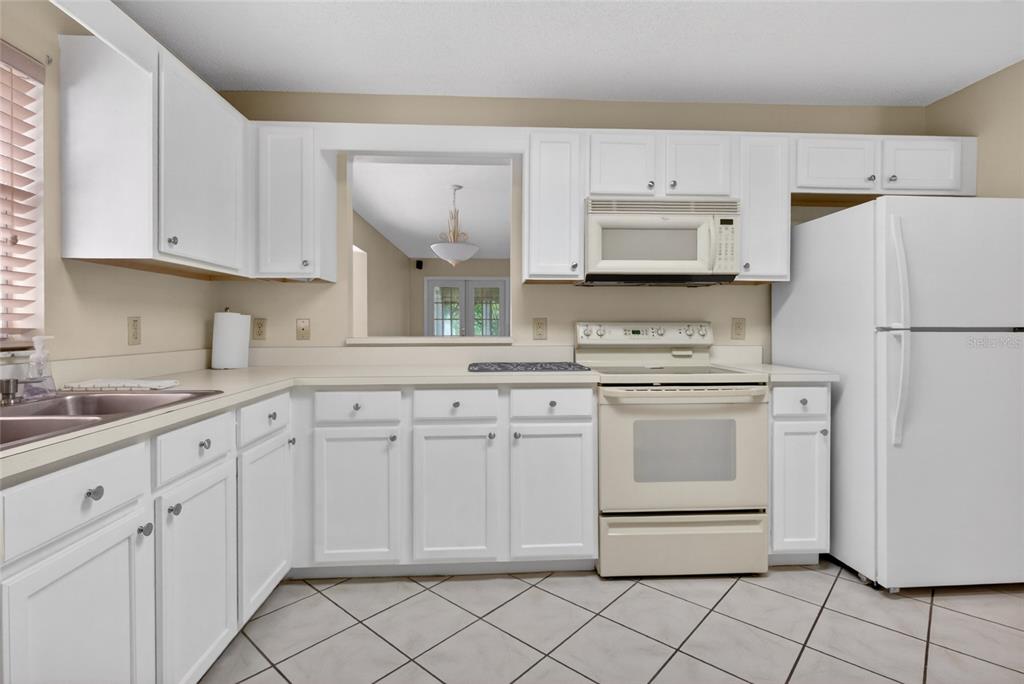 A kitchen with white cabinets, a light-colored stove, a white refrigerator, and tiled floors — 9077 SW 91ST CIRCLE, OCALA, FL