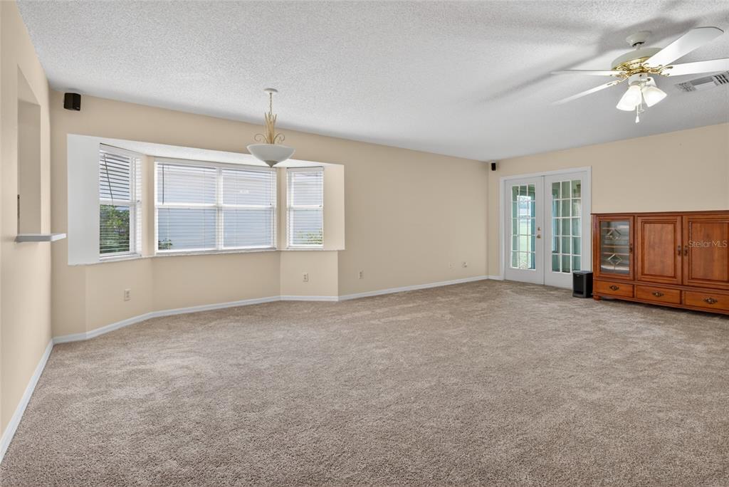 A spacious living room features beige carpet, a bay window, a ceiling fan, and French doors — 9077 SW 91ST CIRCLE, OCALA, FL