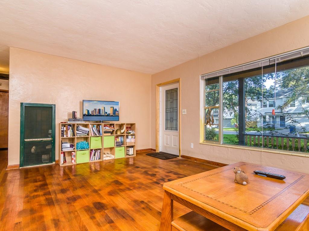 A living room with wood flooring, a bookshelf holding a television, and a large window — 3136 W EUCLID AVENUE, TAMPA, FL