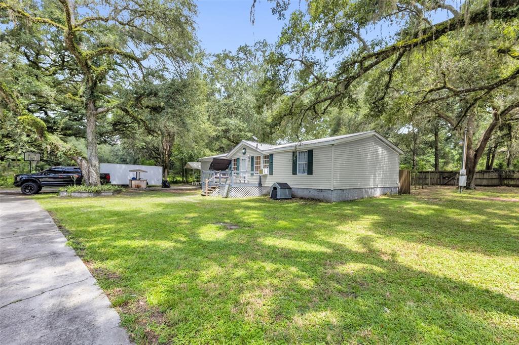 A light-colored manufactured home sits on a grassy lot shaded by large oak trees — 1705 SE 179 PLACE, SUMMERFIELD, FL