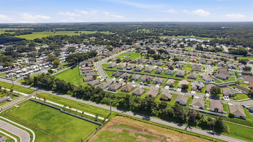 An aerial view shows a suburban neighborhood with single-family homes, green lawns, and nearby roads — 7631 MERCHANTVILLE CIRCLE, ZEPHYRHILLS, FL