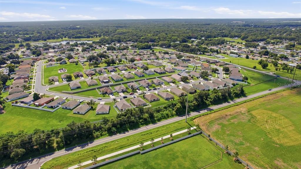 An aerial view shows a suburban neighborhood with single-family homes surrounded by green lawns — 7631 MERCHANTVILLE CIRCLE, ZEPHYRHILLS, FL