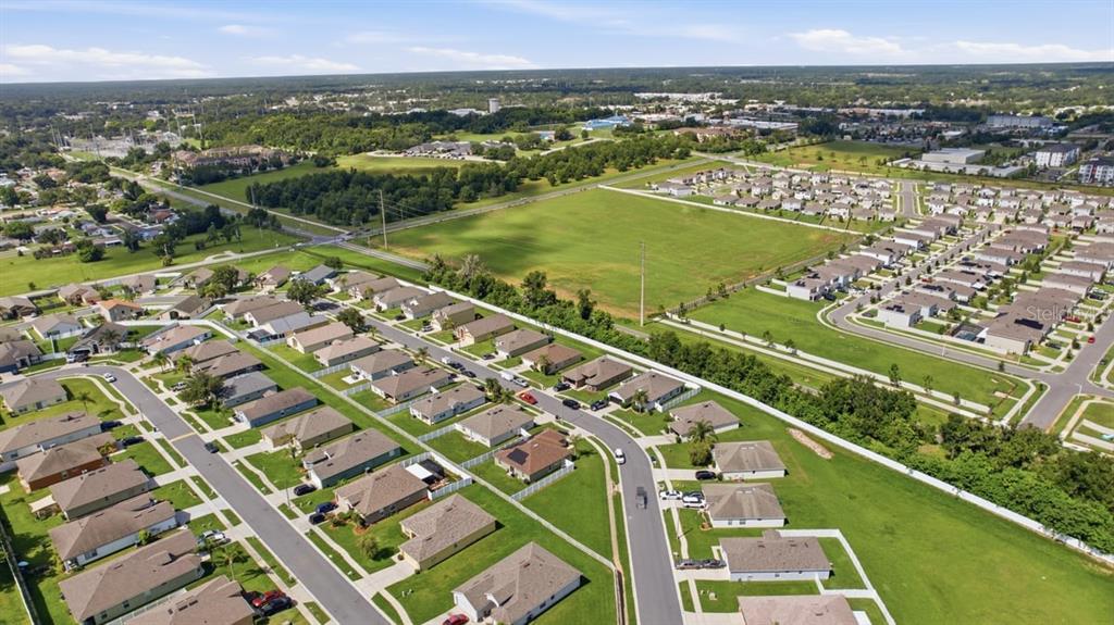 An aerial view shows a suburban neighborhood with houses, streets, and large grassy fields — 7631 MERCHANTVILLE CIRCLE, ZEPHYRHILLS, FL