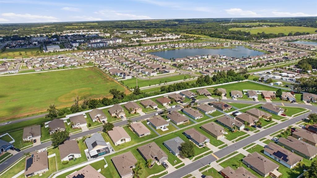 An aerial view shows a suburban neighborhood with many single-family homes and a central lake — 7631 MERCHANTVILLE CIRCLE, ZEPHYRHILLS, FL