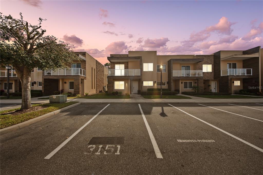 A row of modern townhomes with balconies faces a paved parking lot at sunset — 3151 BRASILIA AVENUE, KISSIMMEE, FL