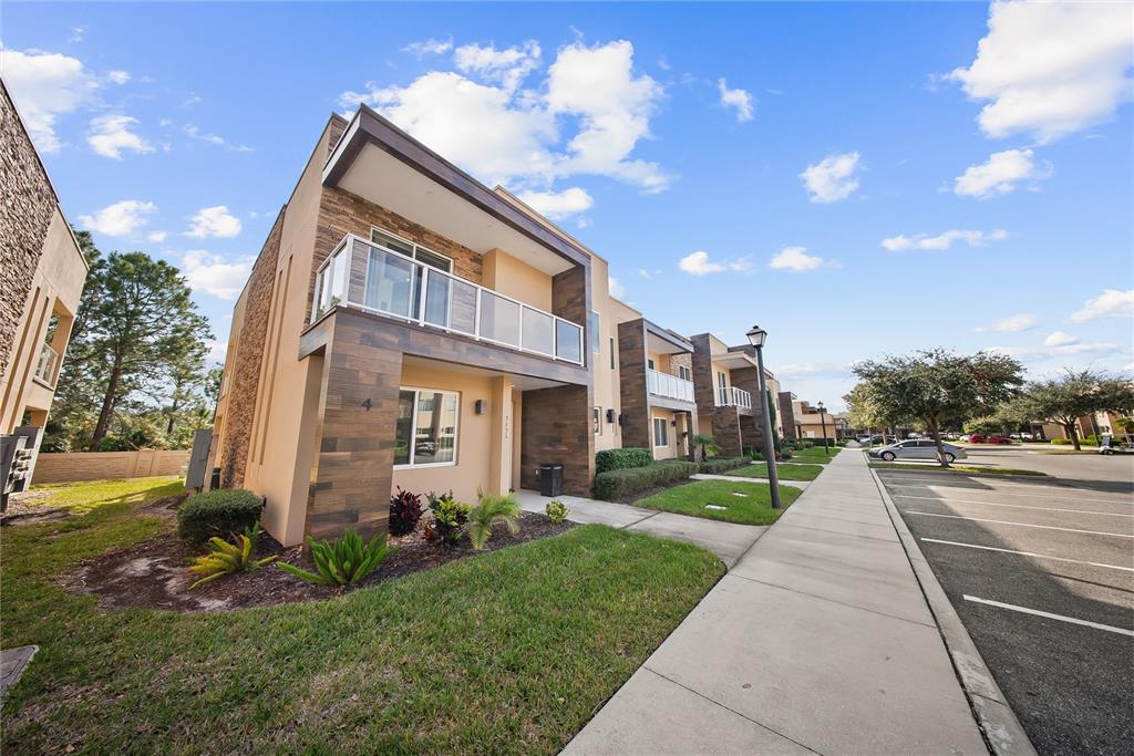 A modern multi-story townhouse exterior features a balcony, wood-look siding, and a paved walkway — 3151 BRASILIA AVENUE, KISSIMMEE, FL