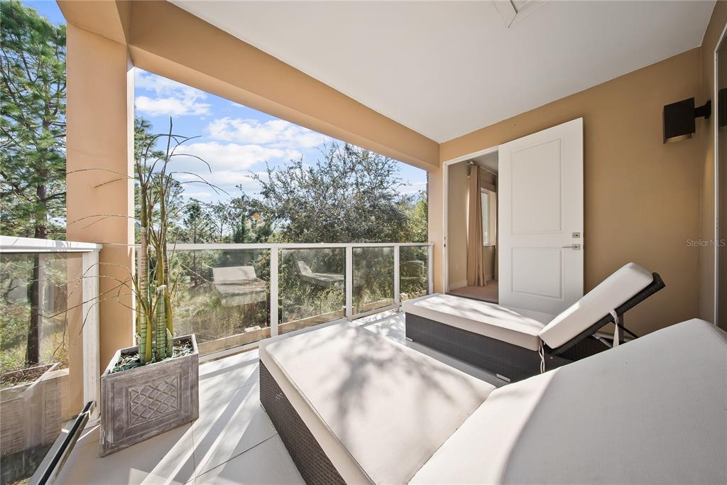 A covered balcony features two lounge chairs, a potted plant, and a glass railing — 3151 BRASILIA AVENUE, KISSIMMEE, FL