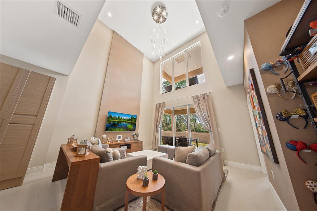 A living room with high ceilings, a chandelier, a television, and a sliding glass door — 3151 BRASILIA AVENUE, KISSIMMEE, FL