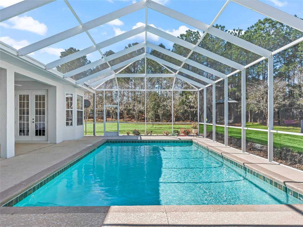 A rectangular swimming pool is enclosed by a white-framed screen structure next to a house — 3030 NW 95TH AVENUE ROAD, OCALA, FL