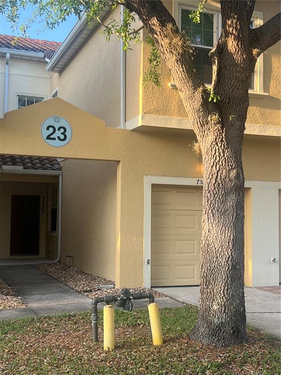 A two-story tan stucco townhouse with a garage, a front entrance, and a large tree — 7523 PELLHAM WAY, KISSIMMEE, FL