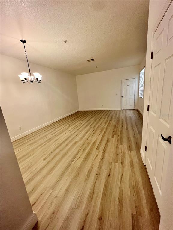 An empty room features light wood-look flooring, white walls, and a hanging chandelier — 7523 PELLHAM WAY, KISSIMMEE, FL