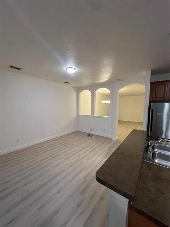 A kitchen counter overlooks an open living area with light wood-look flooring and arched cutouts — 7523 PELLHAM WAY, KISSIMMEE, FL