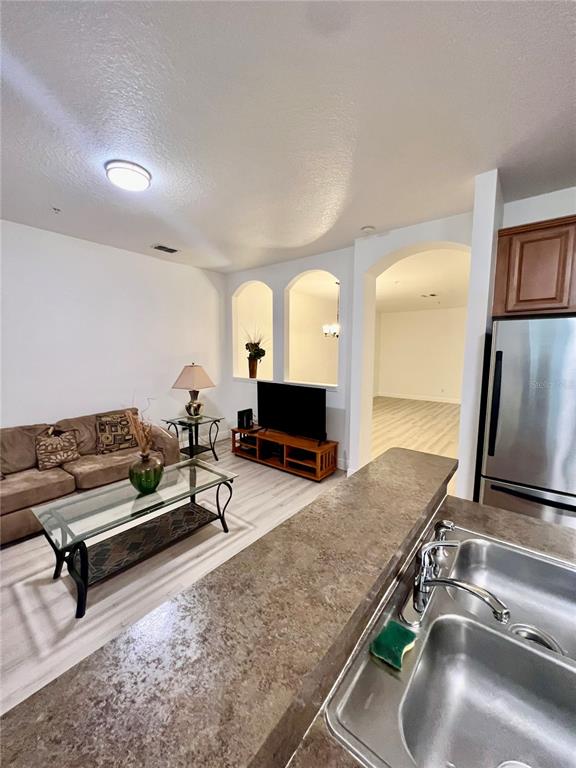 A kitchen counter overlooks a living room with a sofa, television, and arched wall cutouts — 7523 PELLHAM WAY, KISSIMMEE, FL