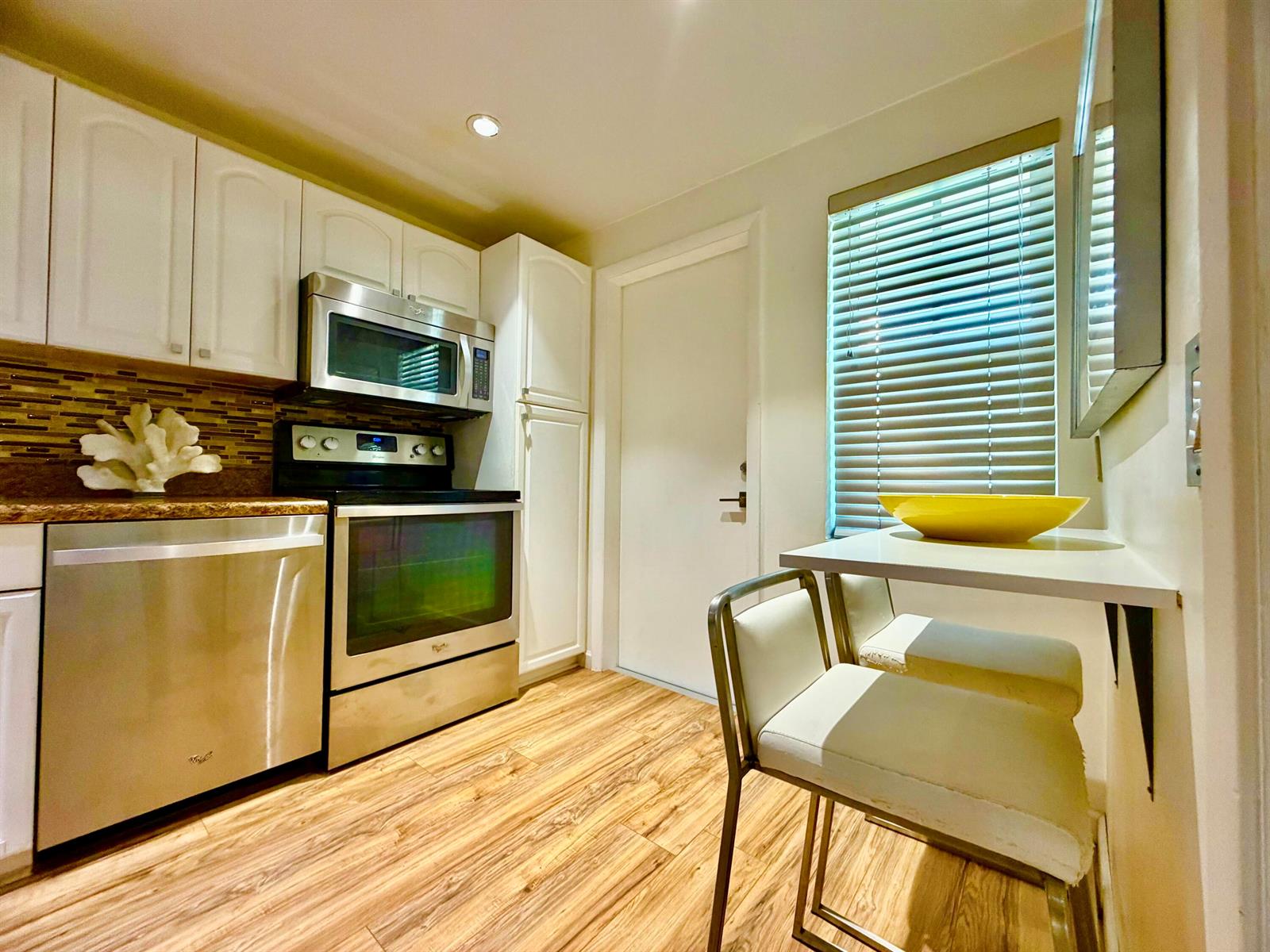 A kitchen with white cabinets, stainless steel appliances, wood-look flooring, and a small breakfast bar — 3100 N Palm Aire Drive # 706, Pompano Beach FL 33069, POMPANO BEACH, FL