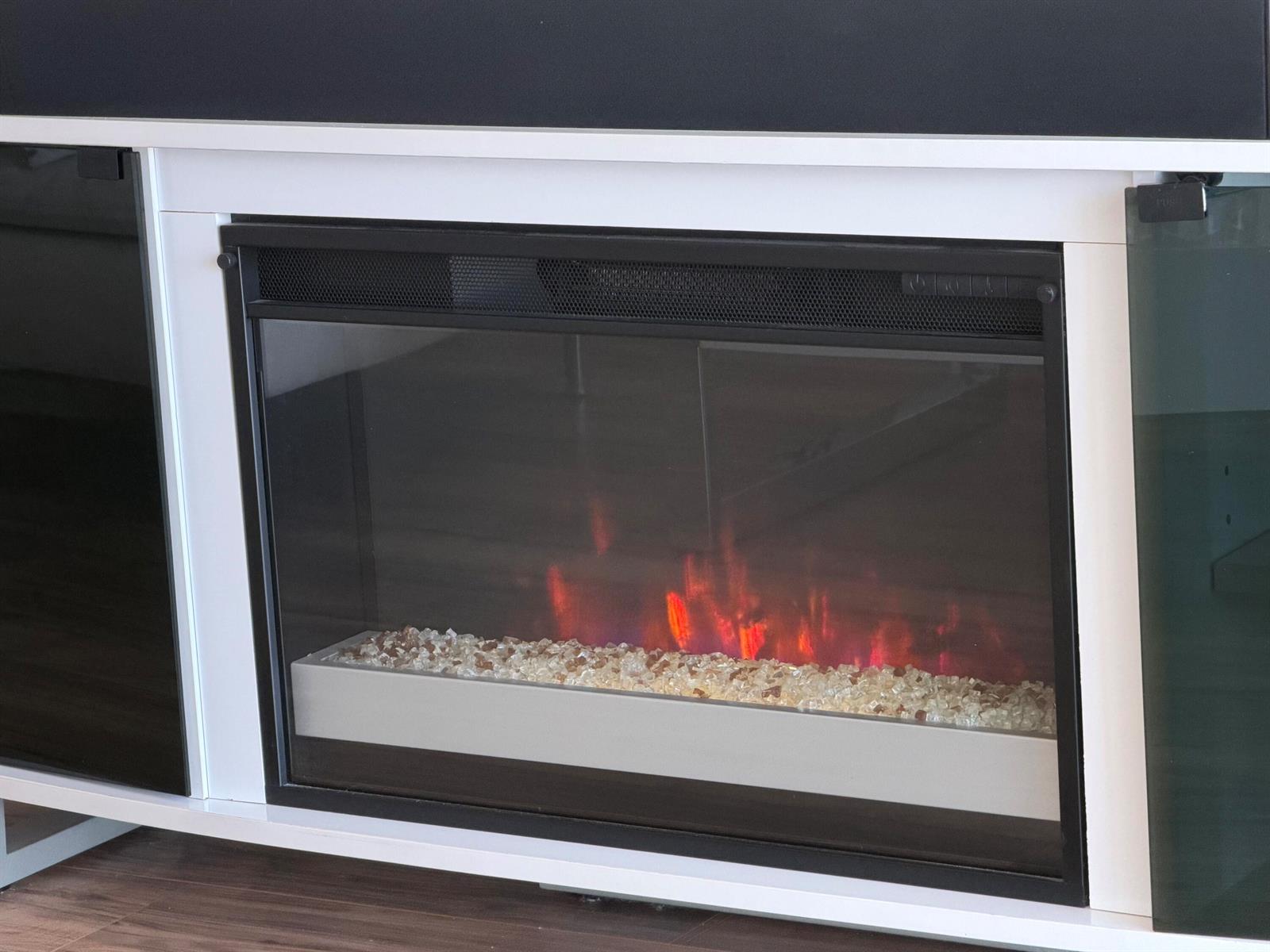 A modern electric fireplace with glass crystals is set within a white media console — 3100 N Palm Aire Drive # 706, Pompano Beach FL 33069, POMPANO BEACH, FL
