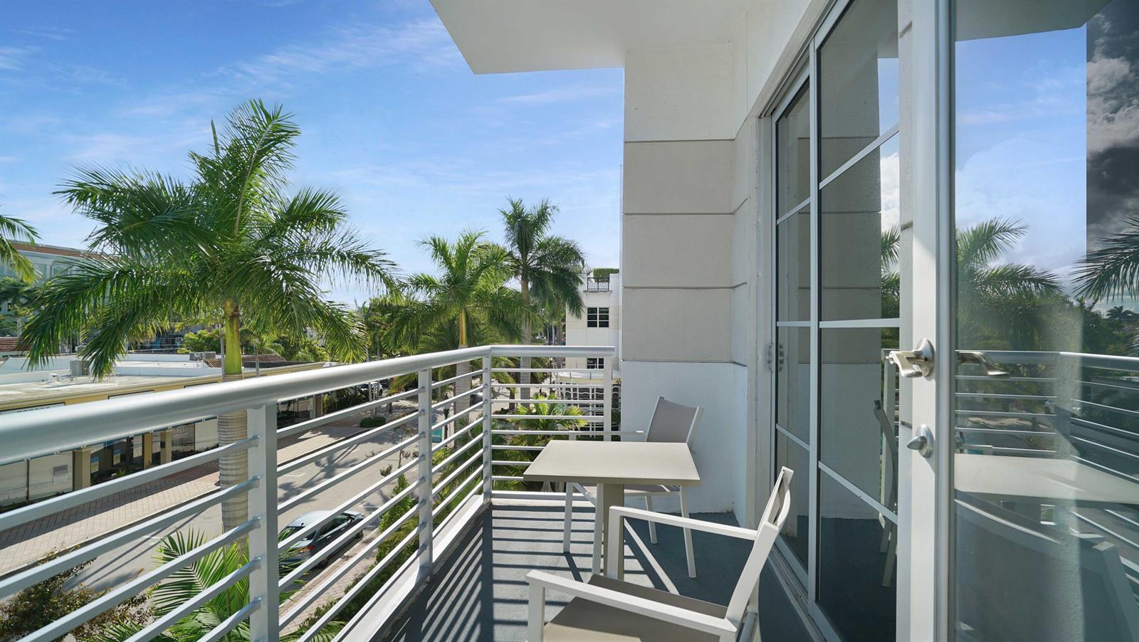 A balcony with a small table and two chairs overlooks a street with palm trees — 155 E Boca Raton Road # 301, Boca Raton FL 33432, BOCA RATON, FL