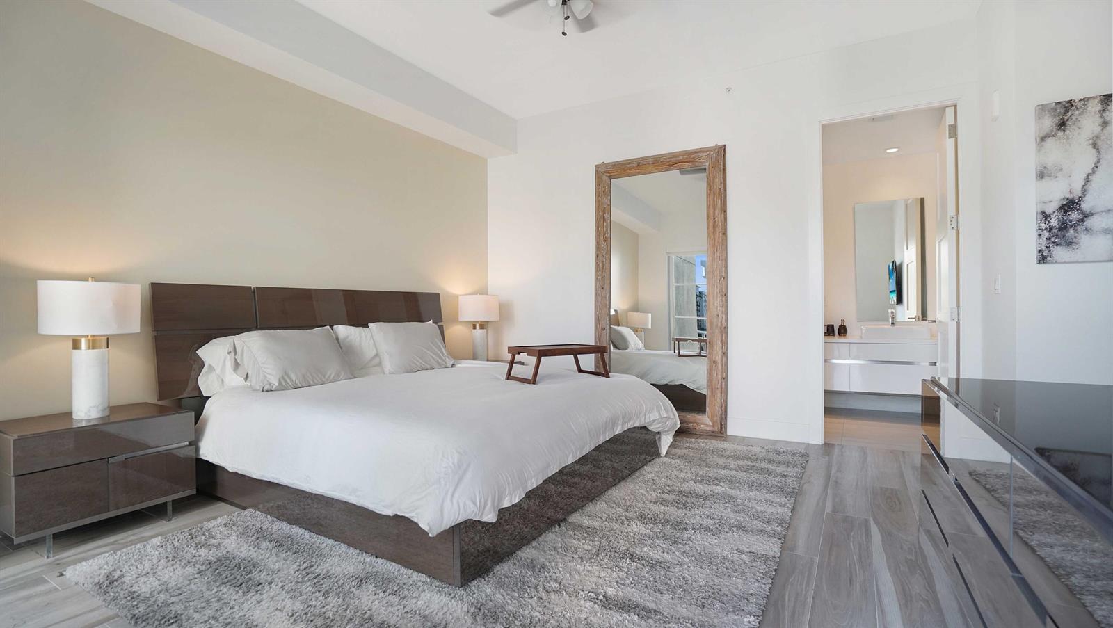 A modern bedroom features a king bed, a large floor mirror, and gray wood flooring — 155 E Boca Raton Road # 301, Boca Raton FL 33432, BOCA RATON, FL
