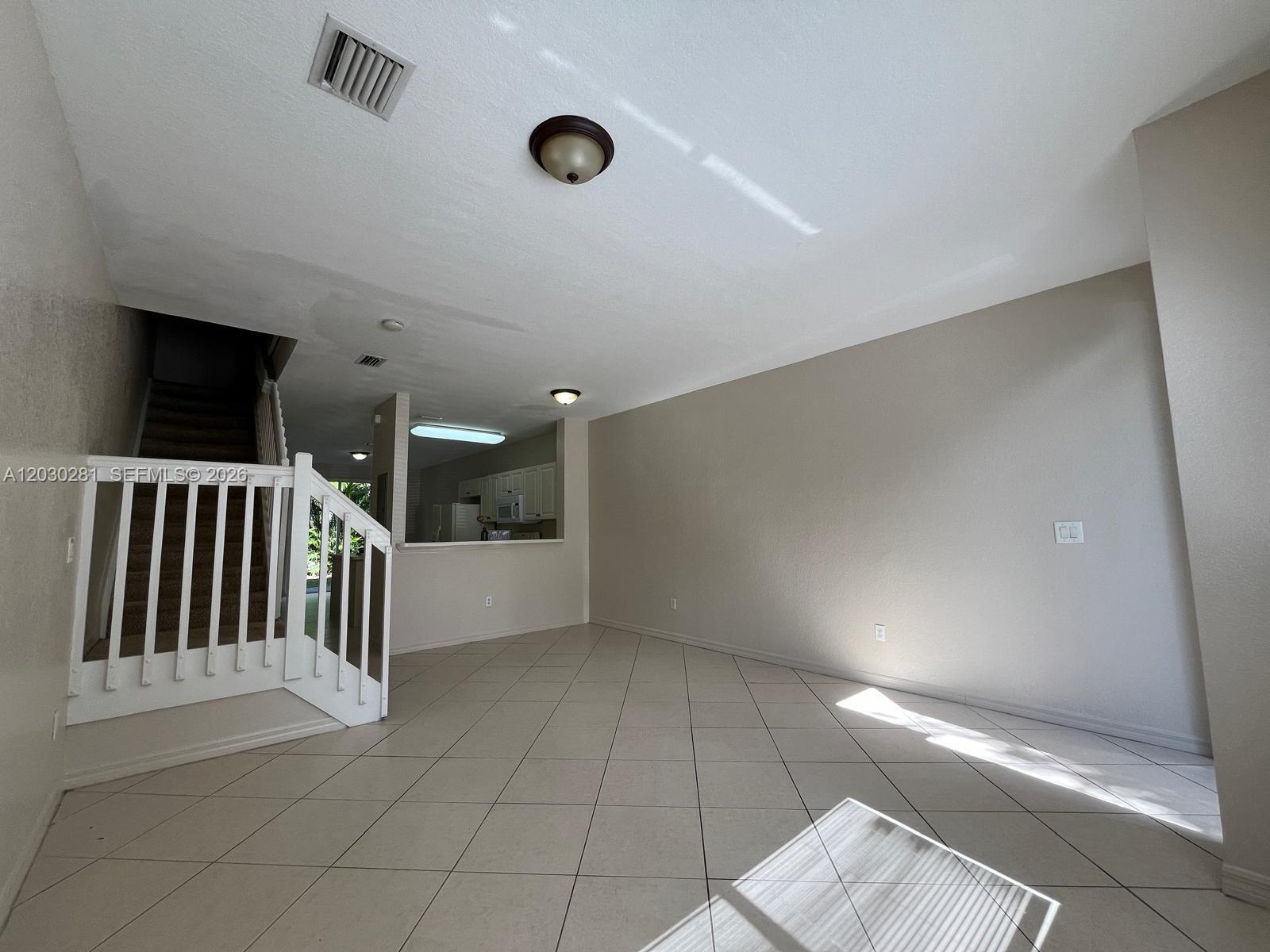 An open living area features tile flooring, a staircase with white railings, and a kitchen pass-through — 1932 Alamanda Way # 1932, Riviera Beach FL 33404, RIVIERA BEACH, FL