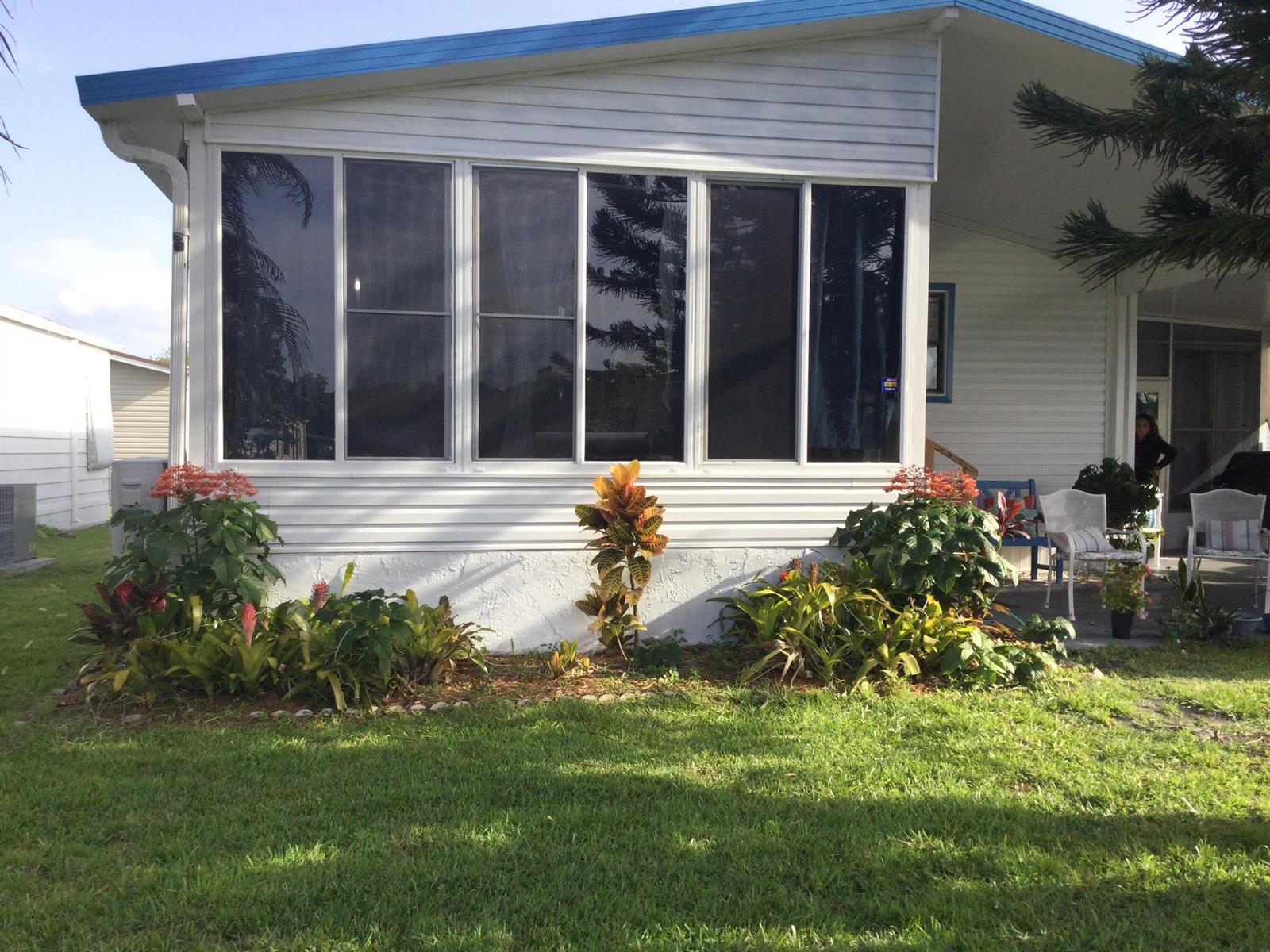 A white mobile home with a large window wall and landscaped garden beds in front — 4748 SE Balsawood Terrace, Stuart FL 34997, STUART, FL