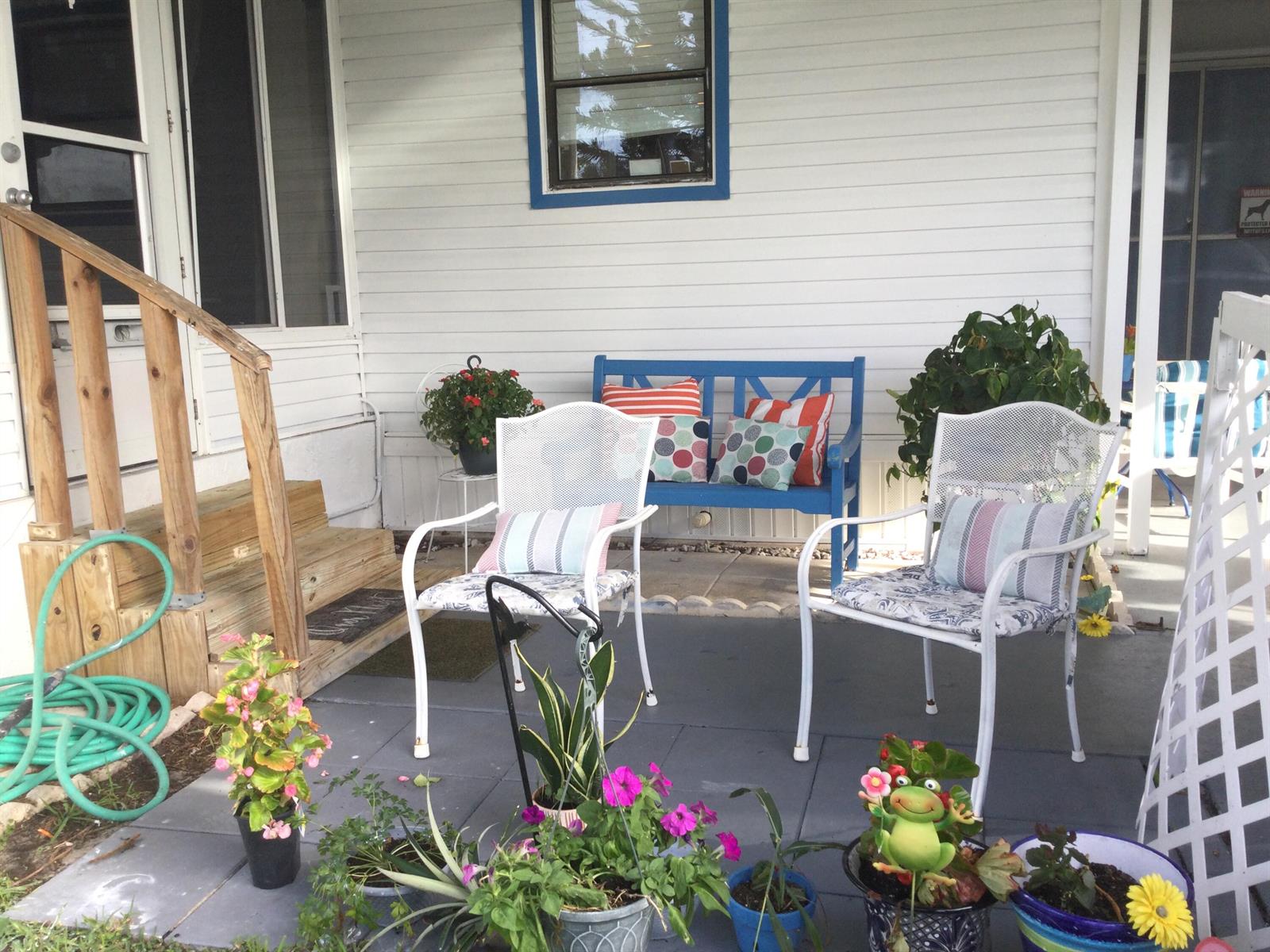 A covered porch features white siding, a blue bench, two white chairs, and potted plants — 4748 SE Balsawood Terrace, Stuart FL 34997, STUART, FL